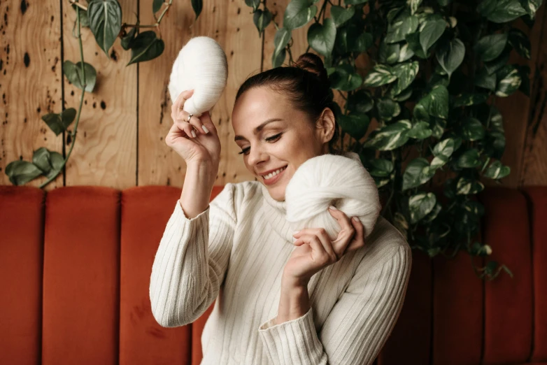 a woman holding a stuffed animal in front of her face, a portrait, by Emma Andijewska, pexels contest winner, brown hair in two buns, wearing a white sweater, photoshoot for skincare brand, ball of yarns all around