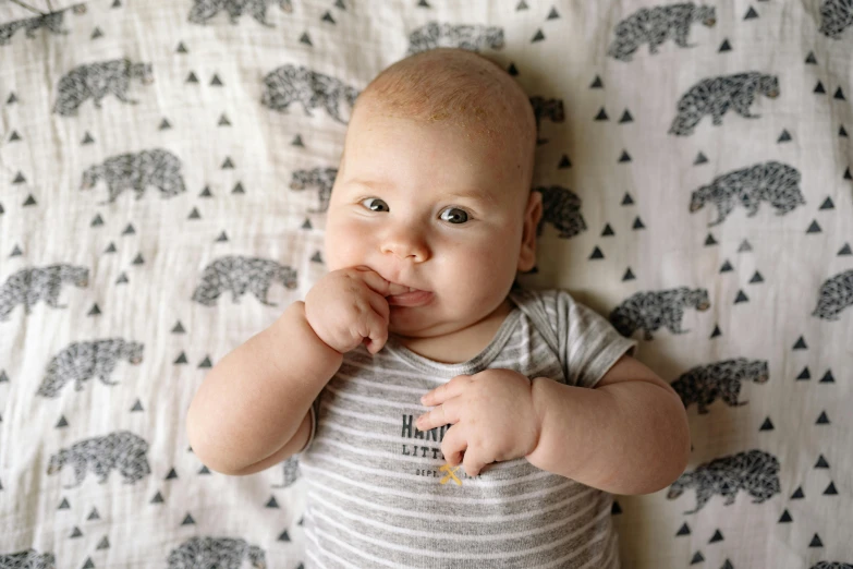 a baby laying on top of a bed covered in a blanket, a portrait, unsplash, happening, hand on his cheek, patterned, grey, finger