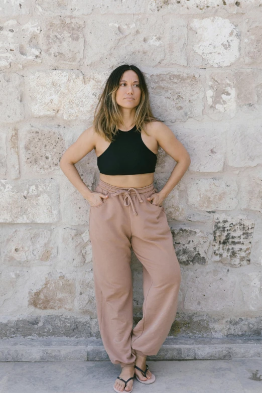 a woman standing in front of a stone wall, featured on instagram, large pants, sandstone, physical : tinyest midriff ever, emma uber