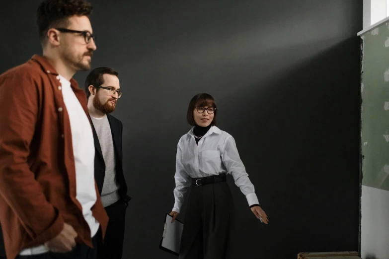 two men and a woman standing in front of a blackboard, pexels contest winner, hyperrealism, wearing a suit and glasses, walking to the right, demna gvasalia, on a gray background