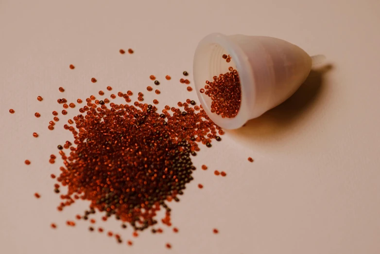 a white cup sitting on top of a table next to a pile of red sprinkles, trending on pexels, pointillism, copper oxide material, detailed glowing red implants, made of beads and yarn, close-up product photo