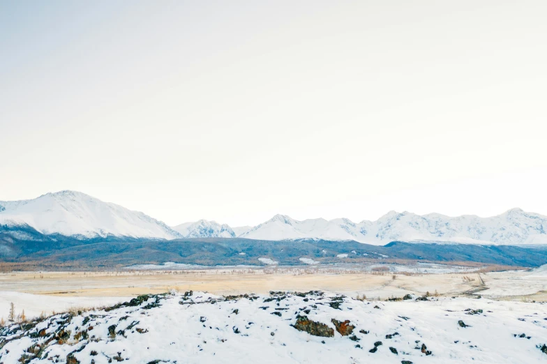 a man riding a snowboard on top of a snow covered slope, an album cover, by Morgan Russell, unsplash, visual art, panorama distant view, new zealand landscape, distant mountains lights photo, overlooking a desolate wasteland