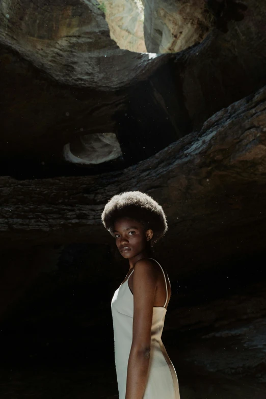 a woman in a white dress standing in a cave, inspired by Carrie Mae Weems, pexels contest winner, afrofuturism, natural hair, black teenage girl, light brown skin, ( ( theatrical ) )