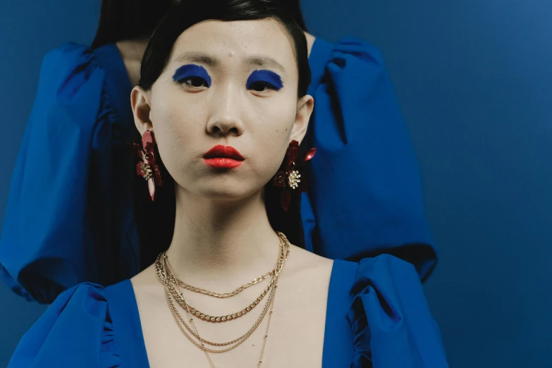 a woman in a blue dress posing for a picture, an album cover, inspired by Wang Meng, trending on pexels, cloisonnism, red jewelry, margiela campaign, multiple earrings, taken with sony alpha 9