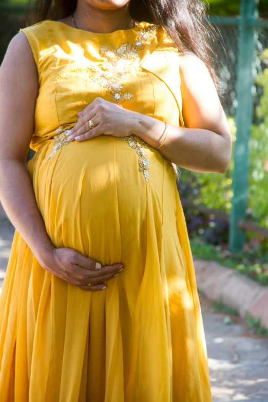 a pregnant woman in a yellow dress poses for a picture, by Elizabeth Durack, pexels, symbolism, detail shot, photograph taken in 2 0 2 0, round-cropped, half image