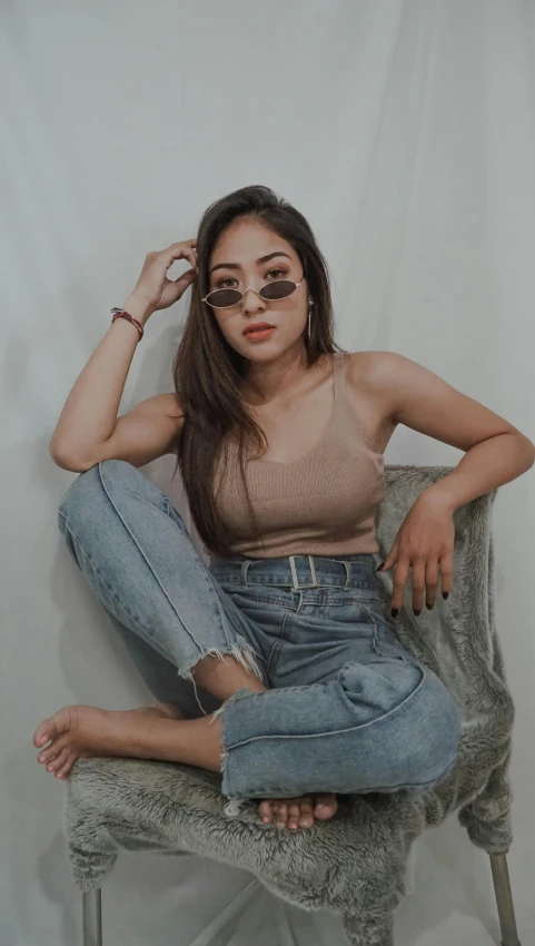 a beautiful young woman sitting on top of a chair, inspired by Natasha Tan, trending on pexels, croptop, ( ( ( wearing jeans ) ) ), wearing shades, low quality photo