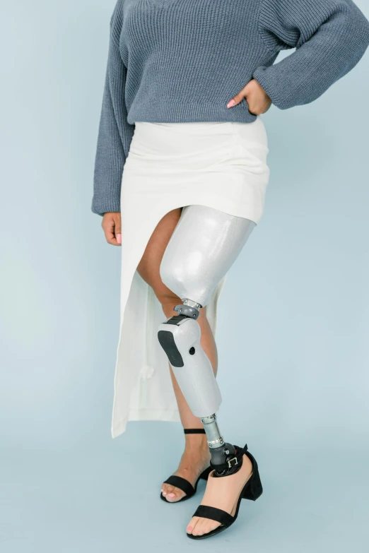 a woman with a prosthetic leg standing in front of a blue background, trending on unsplash, wearing white skirt, grey metal body, surgical impliments, with a white background