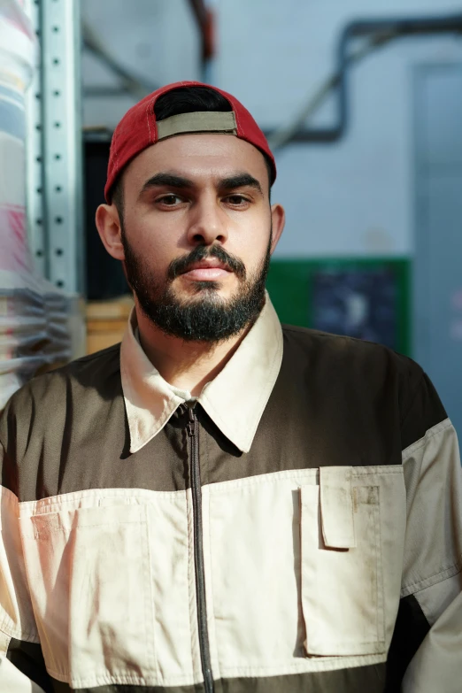 a man with a beard standing in front of a wall, an album cover, unsplash, hurufiyya, wearing a red backwards cap, work clothes, unibrow, in the backrooms