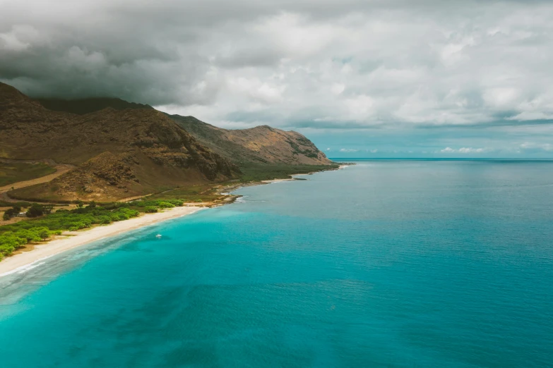 a large body of water next to a lush green hillside, by Ryan Pancoast, unsplash contest winner, hawaii beach, slightly tanned, shades of blue and grey, epic 8 k