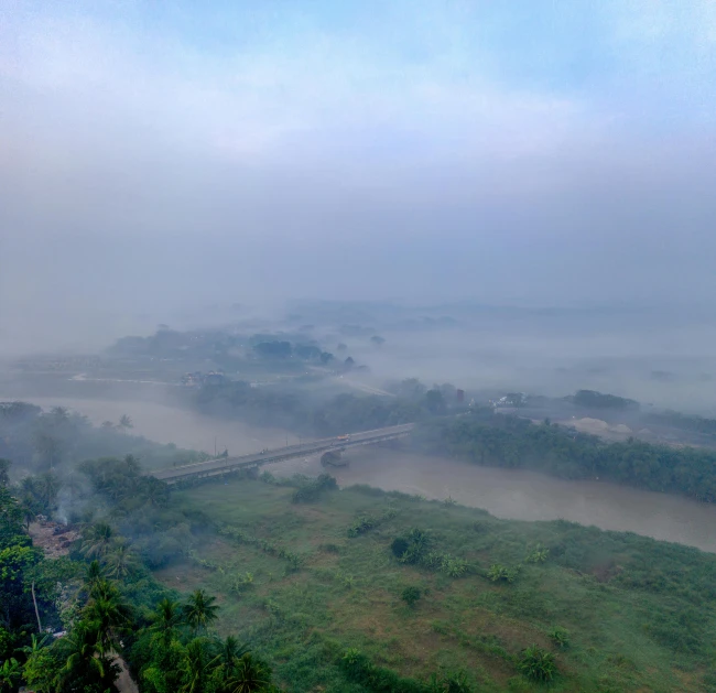 a train traveling down a train track next to a lush green hillside, an album cover, pexels contest winner, hurufiyya, water fog, howrah bridge, panoramic view, hazy morning foggy