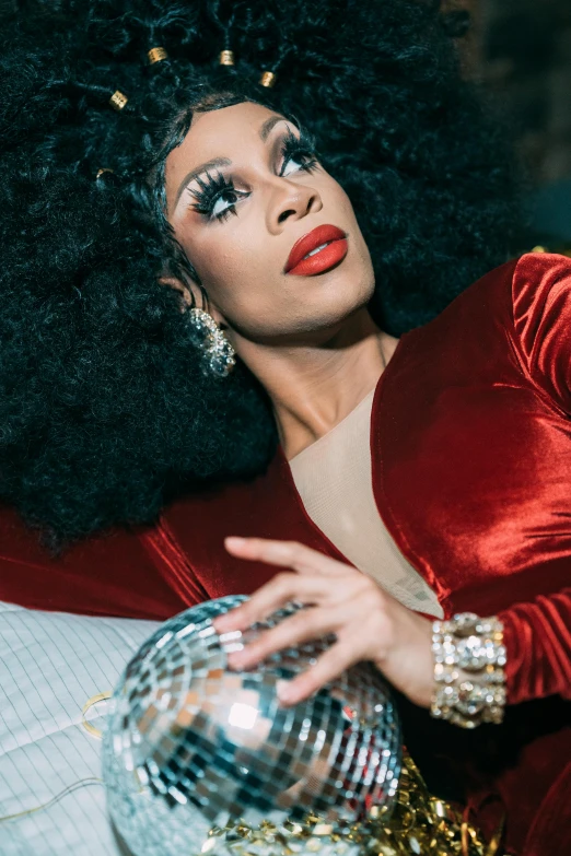 a woman in a red dress holding a disco ball, an album cover, pexels, renaissance, ru paul\'s drag race, lipstick, looking to the side off camera, laying down