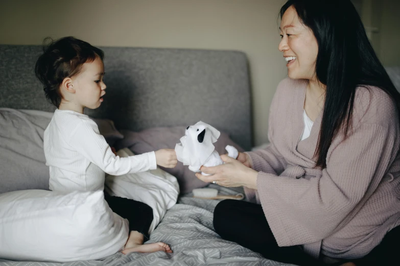 a woman playing with a small child on a bed, pexels contest winner, blue'snappy gifts'plush doll, asian descent, avatar image, grey