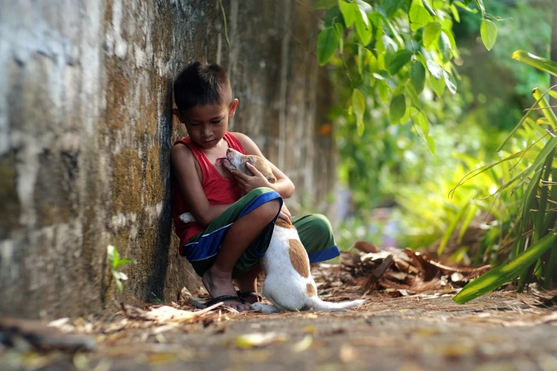 a little girl sitting on the ground with a cat, by Basuki Abdullah, pexels contest winner, sumatraism, teenage boy, subject: dog, gently caressing earth, 15081959 21121991 01012000 4k