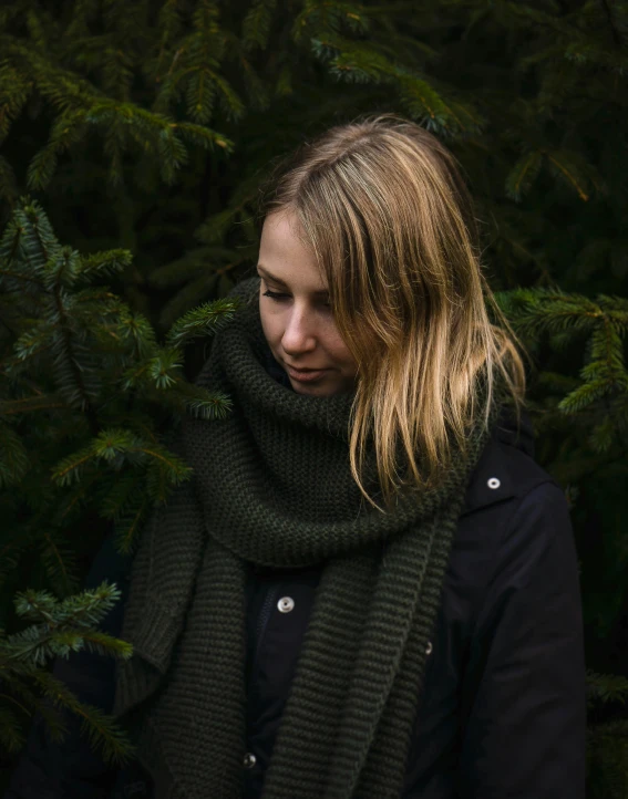 a woman standing in front of a pine tree, a character portrait, inspired by Louisa Matthíasdóttir, pexels contest winner, scarf, dark green, product photo, full shot photograph