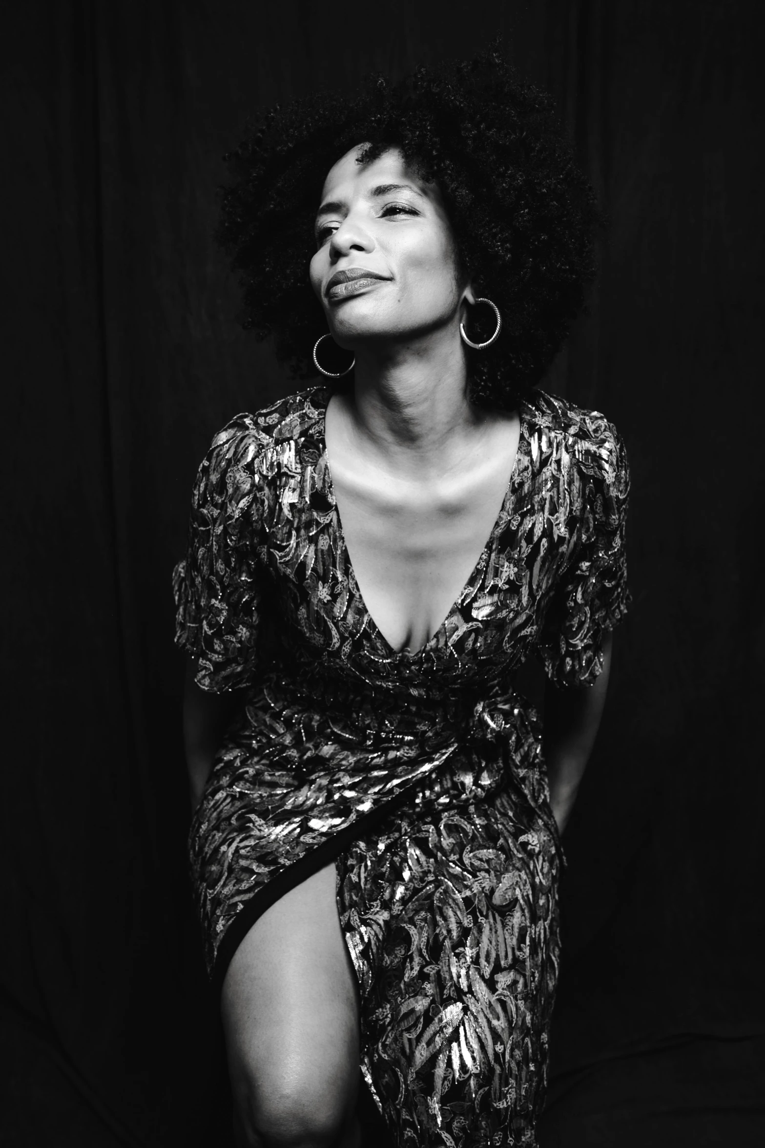 a black and white photo of a woman in a dress, an album cover, pexels, afro hair, actress, casual pose, glowing