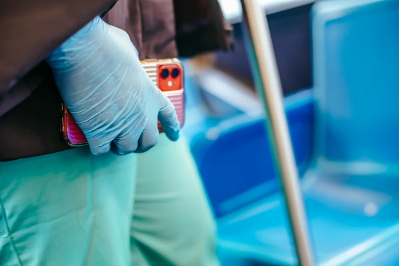 a person wearing gloves and holding a cell phone, colorful medical equipment, bus, back towards camera, holding a cane