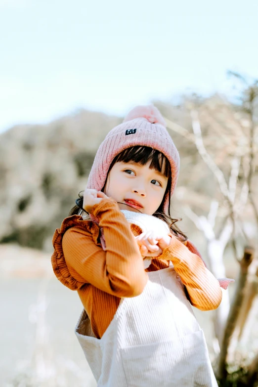 a little girl standing next to a body of water, wearing a beanie, blush, park ji-min, warmer colours