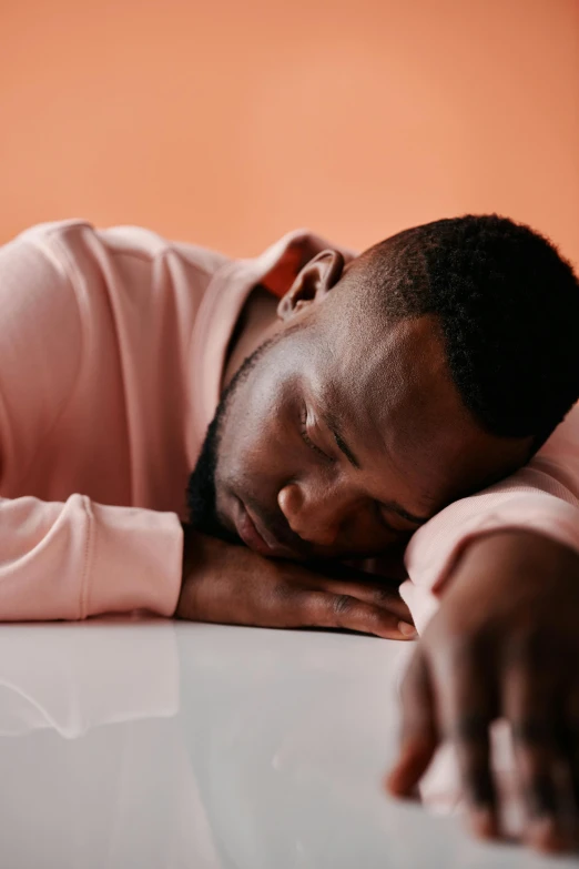 a man resting his head on a table, trending on pexels, happening, in shades of peach, sleeping beauty, man is with black skin, arms down