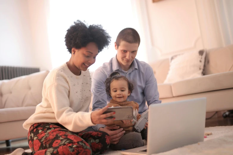 a man and woman sitting on the floor looking at a laptop, a cartoon, by Carey Morris, pexels, portrait of family of three, toddler, diverse, checking her phone