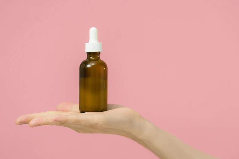 a person holding a brown bottle with a white top, by Olivia Peguero, trending on pexels, pink skin, apothecary, cardboard, petroleum vitamin