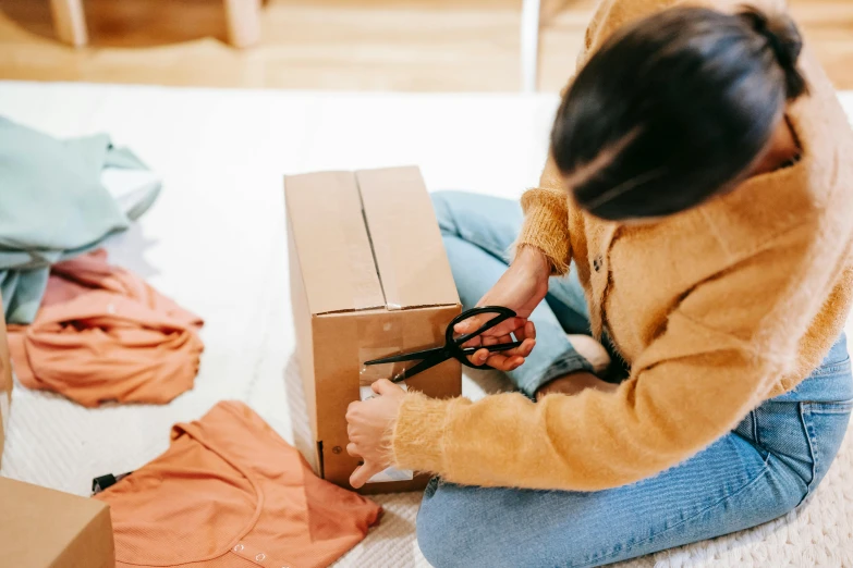 a woman sitting on the floor holding a pair of scissors, pexels contest winner, hurufiyya, delivering packages for amazon, warm color clothes, ebay listing thumbnail, clothes torn apart