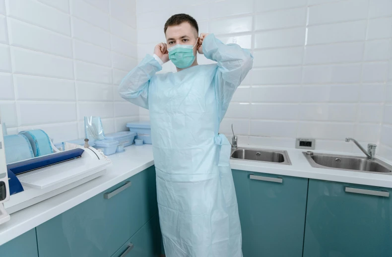 a woman in a surgical gown standing in a kitchen, by Adam Marczyński, pexels contest winner, plasticien, a handsome, nurse costume, white and teal garment, wearing headset