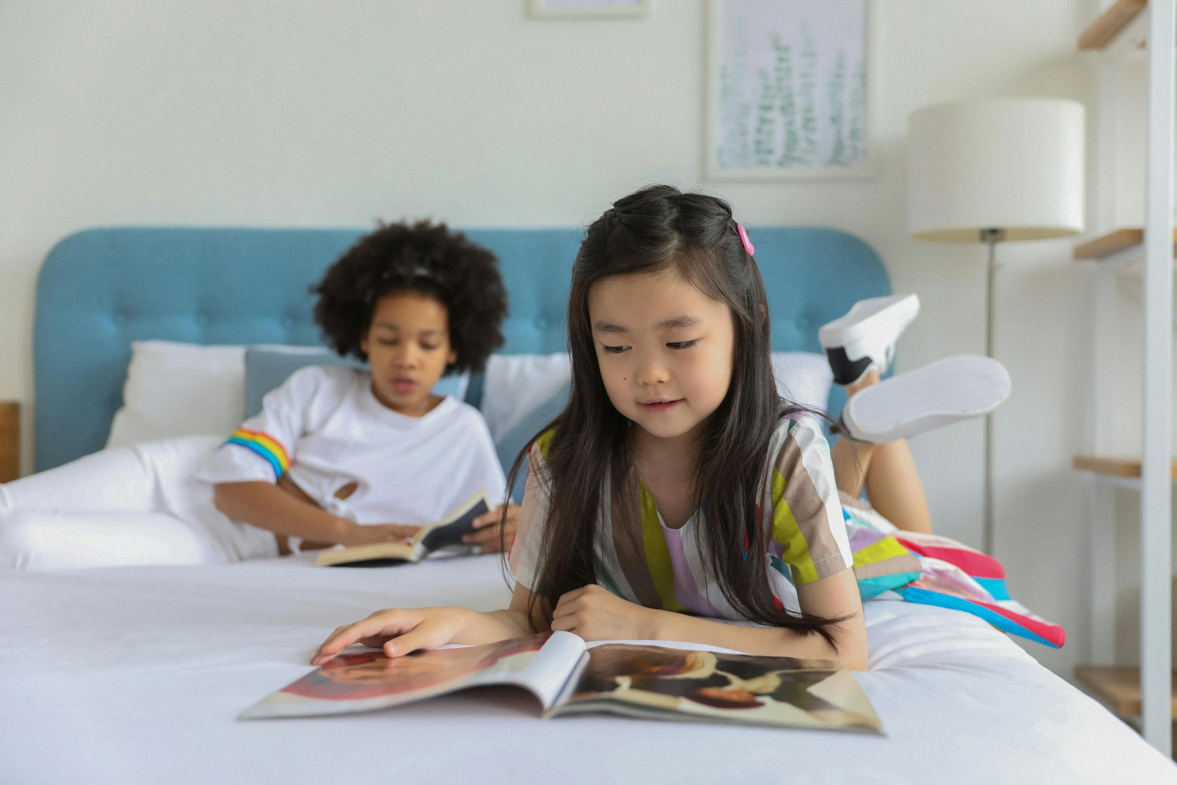 a couple of kids laying on top of a bed, by Julian Allen, pexels contest winner, reading engineering book, young asian girl, bright colour, full length shot