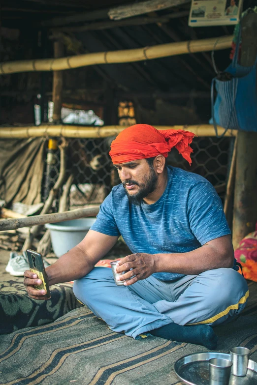 a man sitting on the ground eating food, a portrait, inspired by Steve McCurry, pexels contest winner, rugged ship captain, looking at his phone, indian, wearing farm clothes