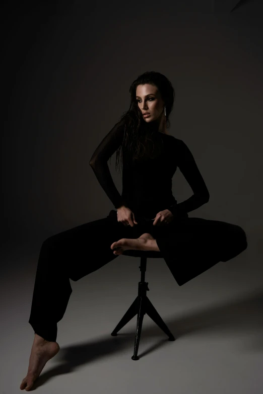 a woman sitting on a stool in a dark room, an album cover, inspired by Marina Abramović, unsplash, arabesque, intimidating pose, black clothing, 2 4 year old female model, dance meditation