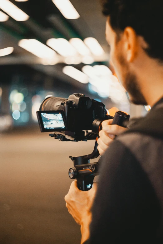 a close up of a person holding a camera, unsplash, video art, cinematic lighting at night, over his shoulder, speed grapher, tripod