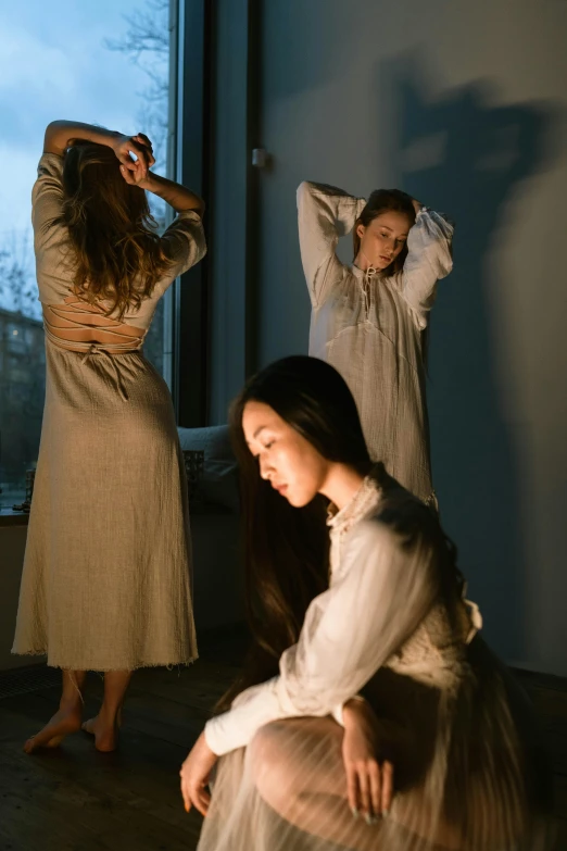 a woman sitting on the floor in front of a window, inspired by Elsa Bleda, pexels contest winner, renaissance, 3 sisters look into the mirror, in long dresses, wearing a light shirt, experimental studio light