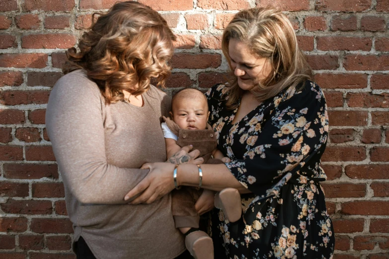 two women and a baby in front of a brick wall, unsplash, brown, holding close, lesbian, full frame image