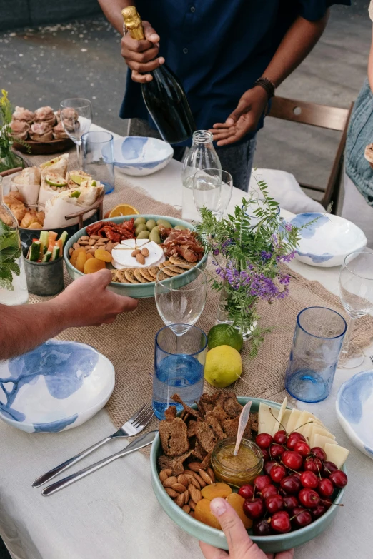 a group of people standing around a table full of food, grey and blue theme, al fresco, picton blue, tabletop