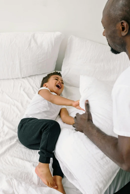 a man and a little girl laying on a bed, earing a shirt laughing, thumbnail, throw pillows, black man