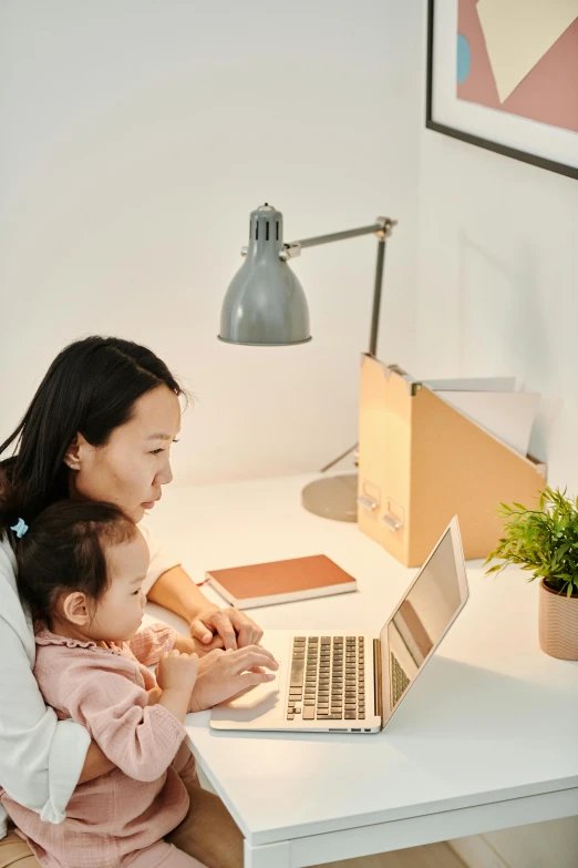 a woman sitting at a desk using a laptop with a child on her lap, pexels contest winner, japanese collection product, sustainable materials, light glow, avatar image