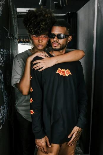 a man and a woman standing next to each other, an album cover, trending on pexels, black arts movement, casual black clothing, flaming eyes, non binary model, long sleeve