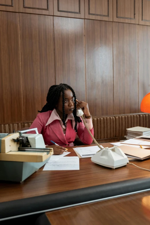 a woman sitting at a desk talking on a phone, lupita nyong'o, circa 1970, an award winning masterpiece, in office