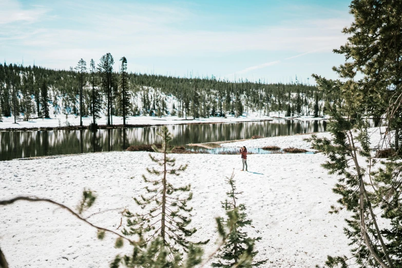 a man standing on top of a sandy beach next to a lake, snow forest, wyoming, instagram post, people walking around