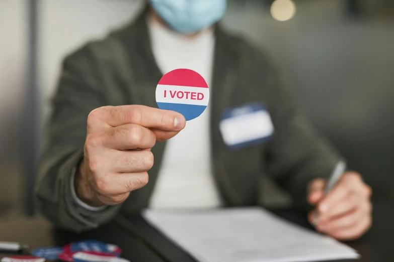 a person wearing a face mask holding a vote sticker, shutterstock, holding a staff, colour photograph, frank moth, thumbnail