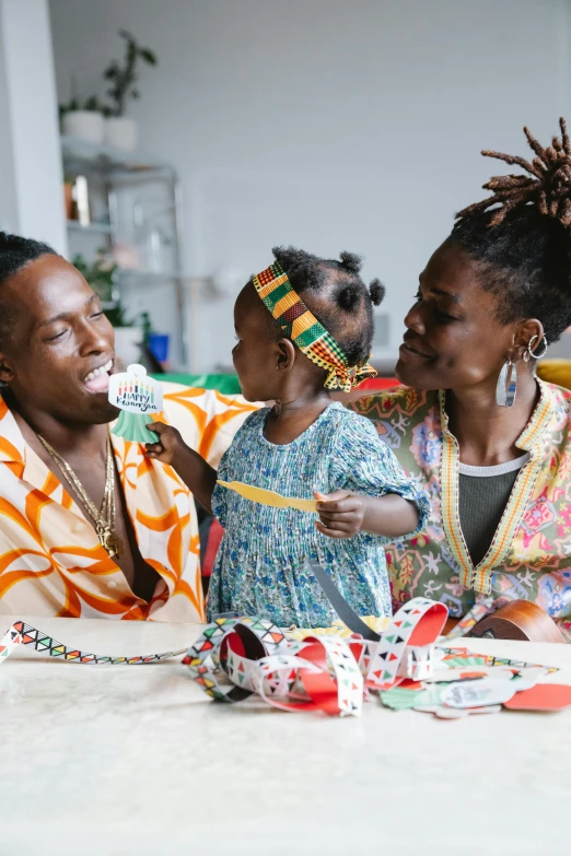 a group of people sitting around a table, by Ingrida Kadaka, pexels contest winner, black arts movement, portrait of family of three, colourful clothing, afro comb, young thug