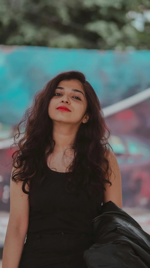 a woman standing in front of a graffiti wall, by Max Dauthendey, pexels contest winner, realism, black wavy hair, indian, panoramic view of girl, red on black