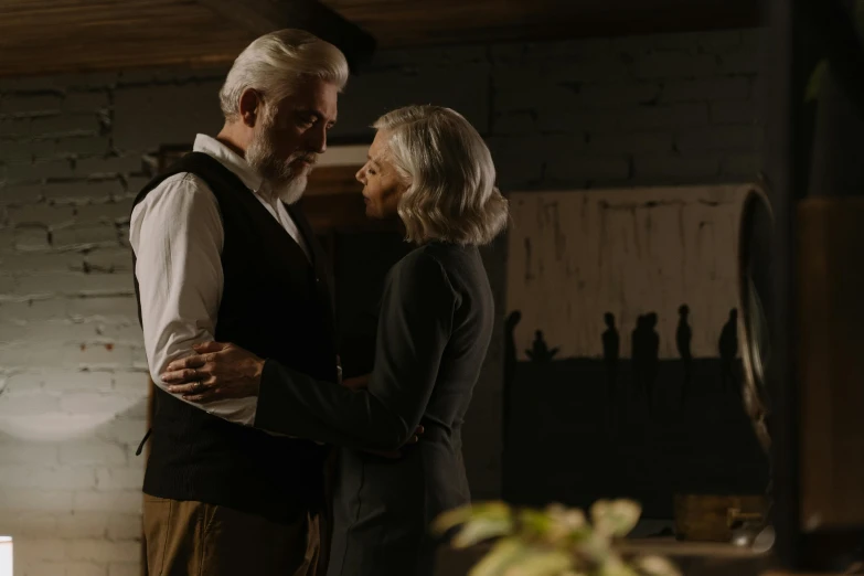 a man and a woman standing next to each other, pexels contest winner, photorealism, white hair and beard, old movie scene, standing in a dimly lit room, view from the side