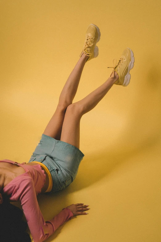 a woman laying on the ground with her legs up, trending on pexels, yellow backdrop, sneakers, pastel clothing, frank moth