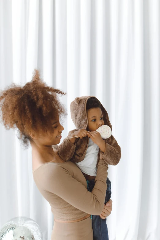 a woman holding a baby in her arms, pexels contest winner, afro comb, brown clothes, high key, 1 2 9 7