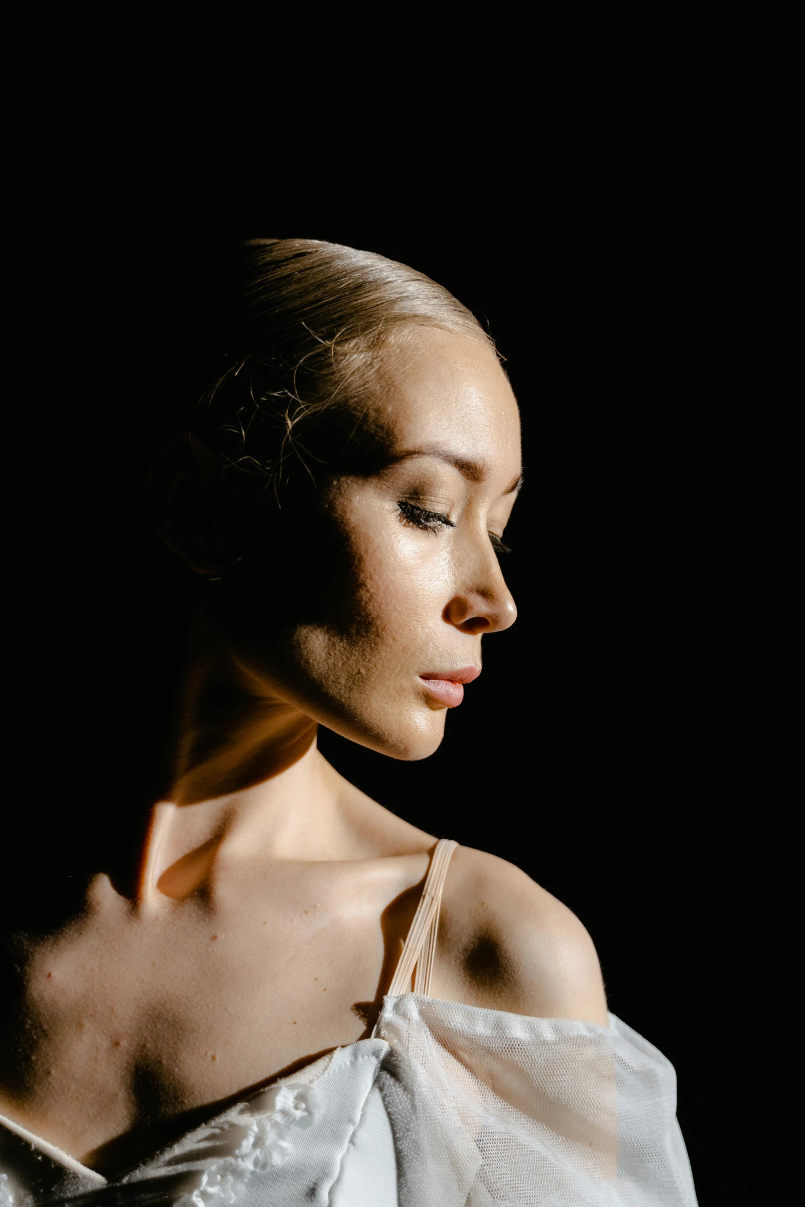 a woman in a white dress with her eyes closed, a portrait, by David Donaldson, unsplash, portrait of a ballerina, spotlight from face, close up of a blonde woman, photographed for reuters