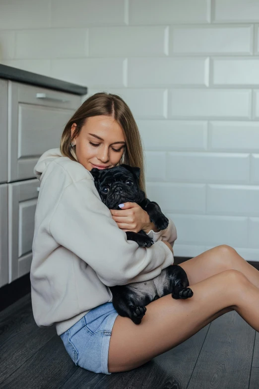 a woman sitting on the floor holding a dog, profile image, holding a pug for a picture, 2019 trending photo, in a kitchen