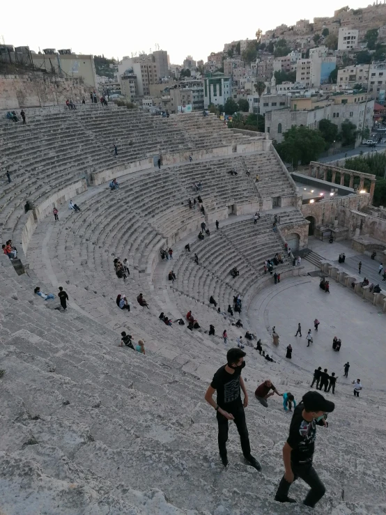 a group of people that are standing in the dirt, an album cover, by Ismail Acar, pexels contest winner, happening, ancient mediterranean city, theater, entire city in view, steps leading down