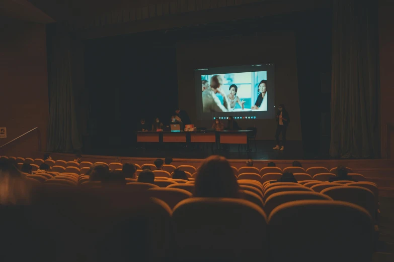 a group of people watching a movie on a big screen, a picture, by Elsa Bleda, unsplash contest winner, video art, sitting in front of a microphone, court session images, ( ( theatrical ) ), color grading