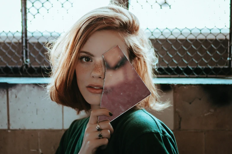 a woman holding a mirror in front of her face, a picture, inspired by Elsa Bleda, trending on pexels, cubism, cute young redhead girl, square face, cut out collage, split hair dye