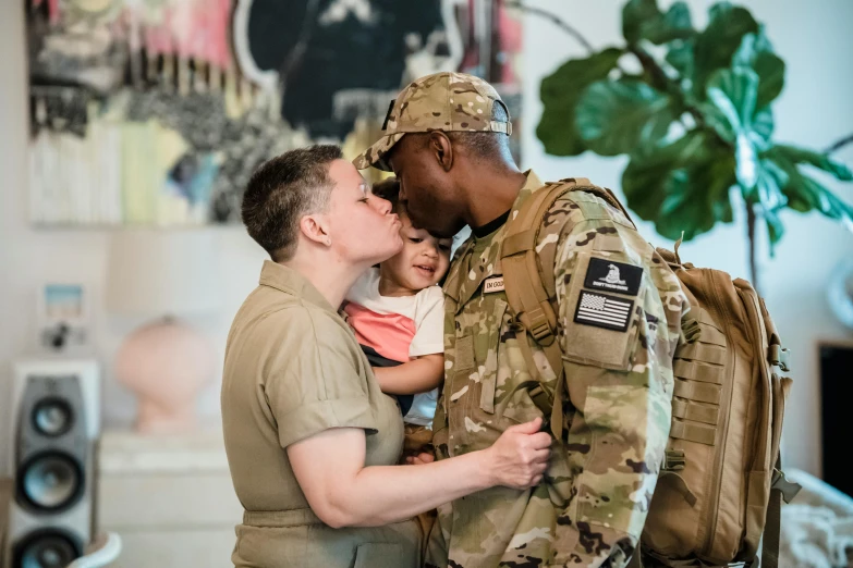 a man in uniform holding a small child, pexels, couple kissing, hgtv, non-binary, wearing camo